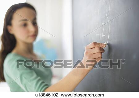 Stock Image - Teenage girl (14-15) writing on blackboard. Fotosearch