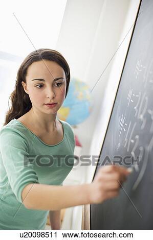 Stock Image - Teenage girl (14-15) writing on blackboard. Fotosearch