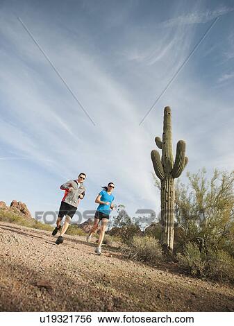 Stock Photograph - USA, Arizona, Phoenix, Mid adult man and young woman jogging on desert. Fotosearch