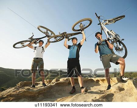 Stock Image - USA, California, Laguna Beach, Mountain bikers on top of hill holding up their bikes. Fotosearch