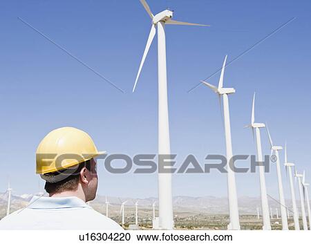 Stock Image - USA, California, Palm Springs, Coachella Valley, San Gorgonio Pass, Man in hard hat looking at wind turbines. Fotosearch