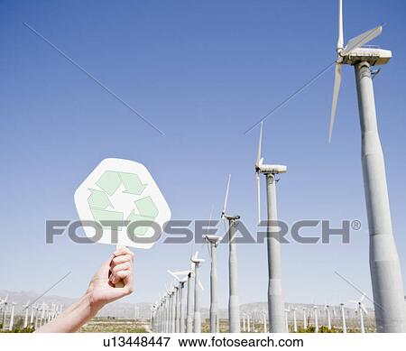Stock Photo - USA, California, Palm Springs, Coachella Valley, San Gorgonio Pass, Woman's hand holding recycling sign against blue sky and wind turbines. Fotosearch