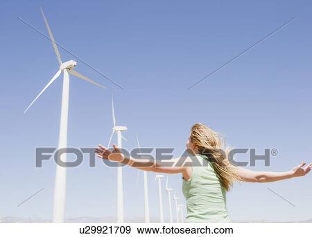 Stock Photo - USA, California, Palm Springs, Coachella Valley, San Gorgonio Pass, Rear view of woman stretching arms and looking at wind turbines . Fotosearch