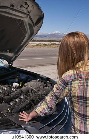 Stock Image - USA, California, Palm Springs, Woman standing in front of broken car in desert. Fotosearch