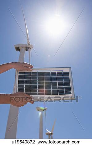 Stock Image - USA, California, Palm Springs, Woman's hands holding solar panel with wind turbines. Fotosearch