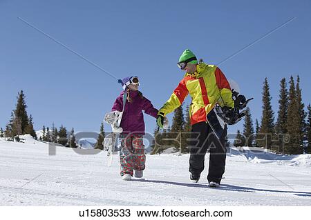 Stock Image - USA, Colorado, Telluride, Father and daughter (10-11) walking with snowboards in winter scenery. Fotosearch