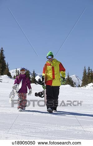 Stock Image - USA, Colorado, Telluride, Father and daughter (10-11) walking with snowboards in winter scenery. Fotosearch
