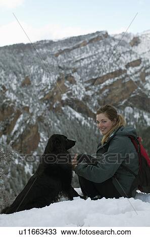 Stock Image - USA, Colorado, young woman and dog sitting on snowy hill. Fotosearch