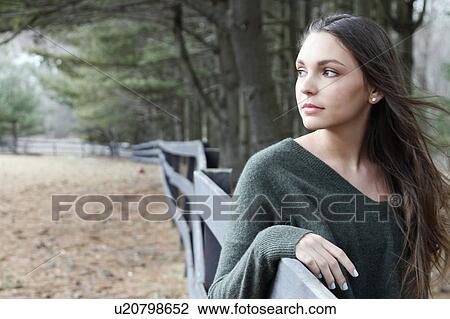 Stock Image - USA, New Jersey, Califon, Teenage girl (16-17) standing near fence and looking away, portrait. Fotosearch