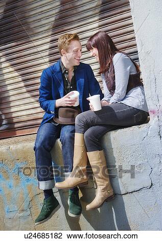 Stock Image - USA, New Jersey, Jersey City, young couple sitting on wall. Fotosearch