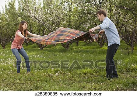 Stock Photography - USA, Utah, Provo, Young couple holding blanket in orchard. Fotosearch