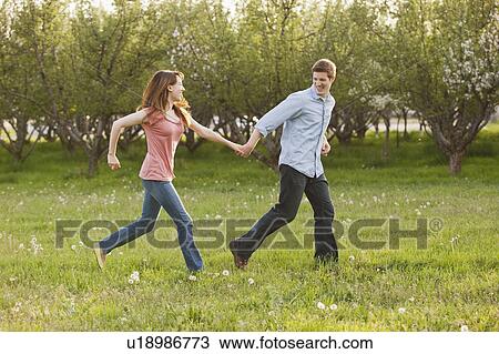 Stock Image - USA, Utah, Provo, Young couple running through orchard. Fotosearch
