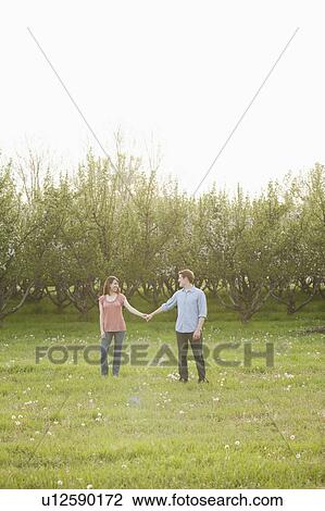 Stock Image - USA, Utah, Provo, Young couple walking through orchard. Fotosearch