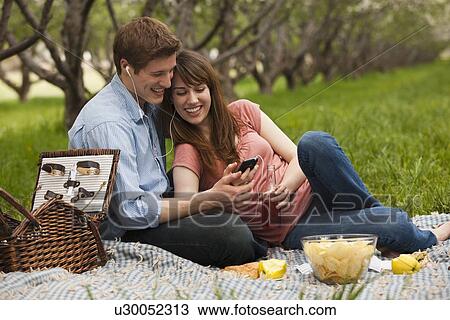 Stock Image - USA, Utah, Provo, Young couple with mp3 player in orchard. Fotosearch