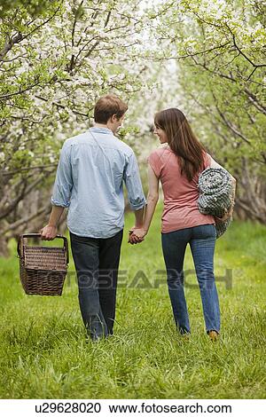 Stock Image - USA, Utah, Provo, Young couple with picnic basket in orchard. Fotosearch