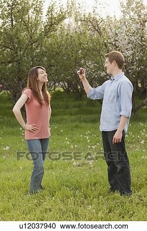 Stock Image - USA, Utah, Provo, Young man photographing young woman in orchard. Fotosearch