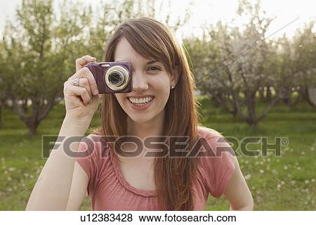 USA, Utah, Provo, Young woman holding digital camera in orchard View Large Photo Image Stock Photo - USA, Utah, Provo, Young woman holding digital camera in orchard. Fotosearch