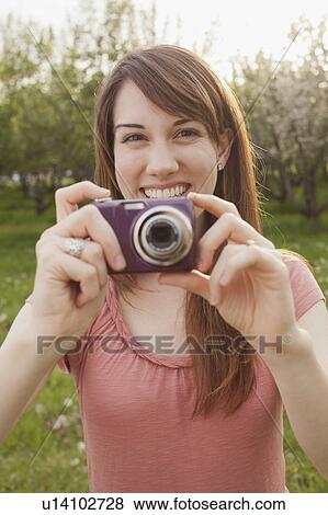Stock Photo - USA, Utah, Provo, Young woman holding digital camera in orchard. Fotosearch
