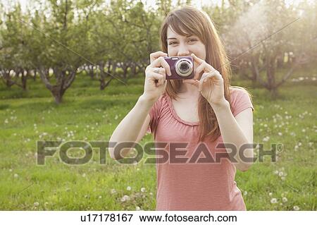 Stock Photo - USA, Utah, Provo, Young woman holding digital camera in orchard. Fotosearch
