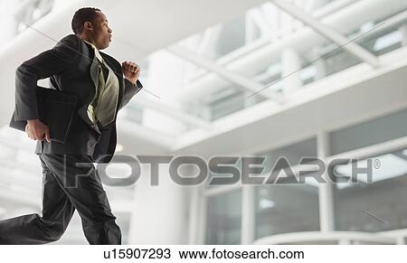 Stock Image - USA, Utah, Salt Lake City, Young businessman running in office building. Fotosearch