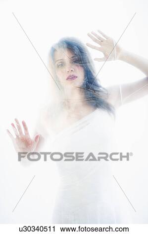 Stock Image - Young attractive woman looking from behind white sheet. Fotosearch