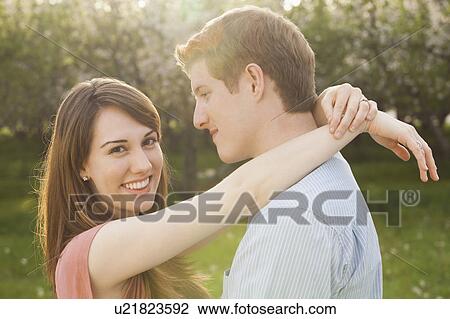 Stock Image - Young couple embracing in orchard. Fotosearch