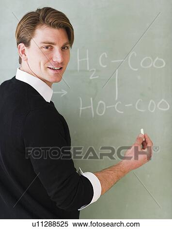 Stock Photography - Young teacher writing equation on blackboard. Fotosearch