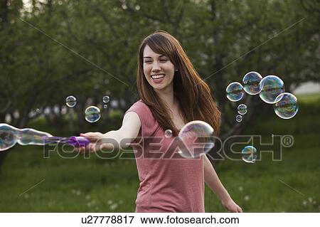Young woman blowing bubbles in orchard View Large Photo Image Stock Photo - Young woman blowing bubbles in orchard. Fotosearch