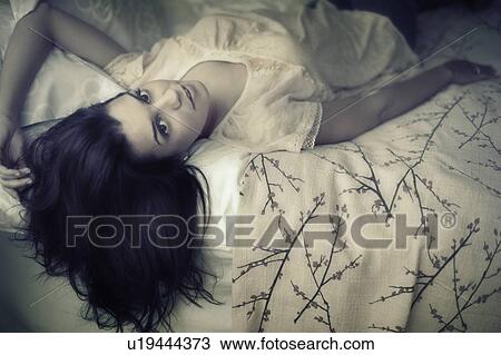 Stock Image - Young woman daydreaming in bed. Fotosearch