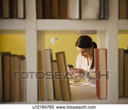 Young woman text messaging in library View Large Photo Image Stock Image - Young woman text messaging in library. Fotosearch