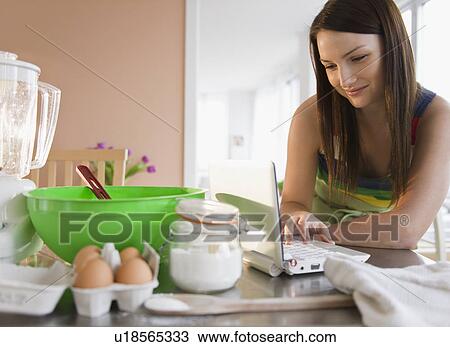 Young woman using laptop at kitchen table View Large Photo Image Stock Image - Young woman using laptop at kitchen table. Fotosearch