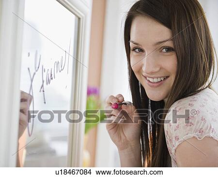 Picture - Young woman writing on mirror with lipstick. Fotosearch