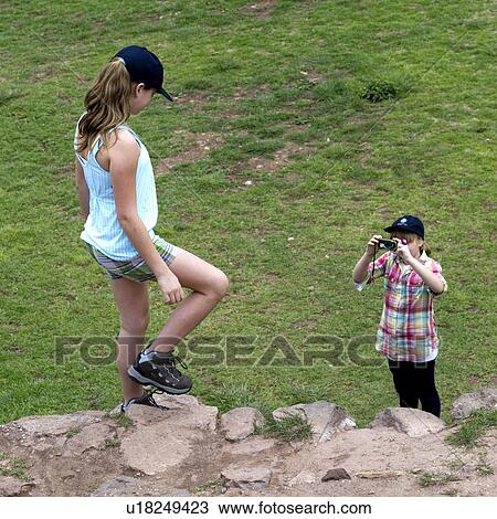 Stock Image - Girl taking picture of her friend with a camera at Incan terraces, Moray, Machu Picchu, Cusco Region, Peru. Fotosearch