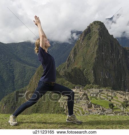 Stock Photography - Teenage girl doing Warrior 1 pose with The Lost City of The Incas in the background, Machu Picchu, Cusco Region, Peru. Fotosearch