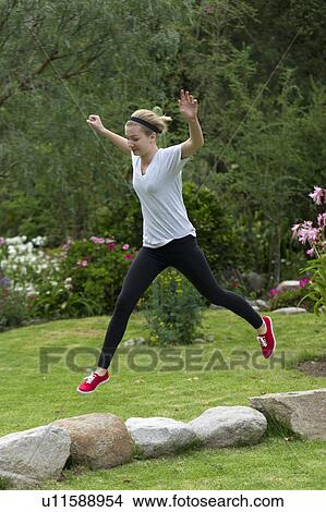 Picture - Teenage girl leaping over rocks in the lawn of Willka Tika Guesthouse, Willka Tika, Sacred Valley, Cusco Region, Peru. Fotosearch