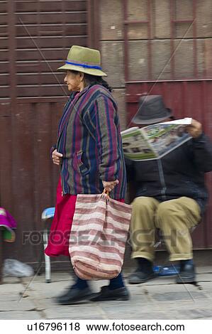 Stock Photo - Woman carrying a bag and walking in a street, Sacred Valley, Cusco Region, Peru. Fotosearch