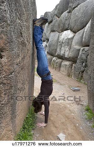 Stock Photograph - Woman doing a handstand in a narrow alley, Sacsayhuaman, Sacred Valley, Cusco Region, Peru. Fotosearch