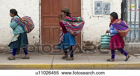 Stock Photography - Women carrying bundles walking on a sidewalk, Pisac, Sacred Valley, Cusco Region, Peru. Fotosearch