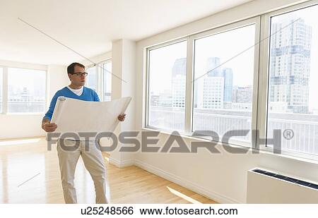 Stock Photograph - Architect reading blueprint in new office. Fotosearch