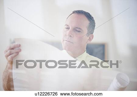 Stock Photograph - Architect reading blueprint in office. Fotosearch