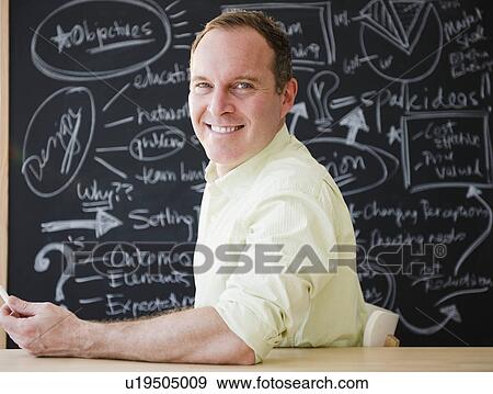 Businessman sitting at table against blackboard View Large Photo Image Stock Photo - Businessman sitting at table against blackboard. Fotosearch