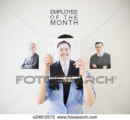Stock Image - Businesswoman holding photos of men to her face. Fotosearch