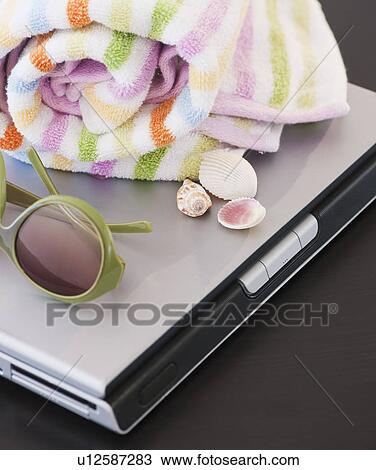 Stock Image - Close up of beach towel and sunglasses on laptop. Fotosearch