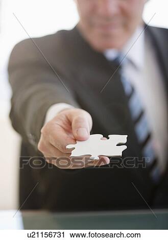 Stock Image - Close up of Businessman holding jigsaw piece. Fotosearch