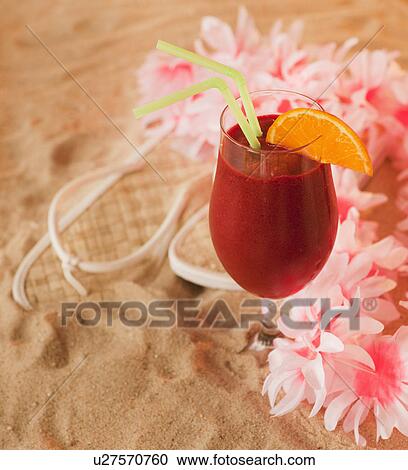 Stock Image - Close up of frozen drink and lei on sand. Fotosearch