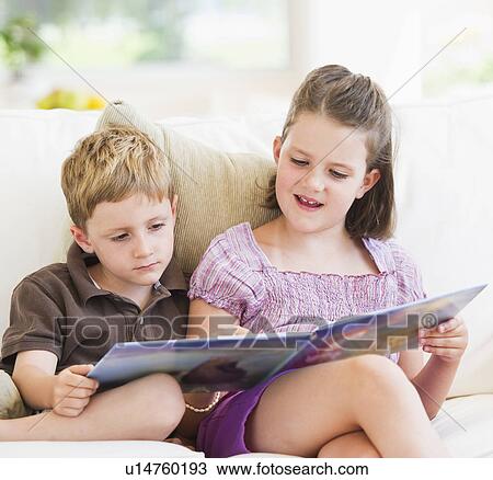Stock Image - Close up of girl (6-7) and boy (4-5) reading book on sofa. Fotosearch