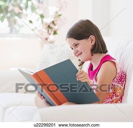 Stock Image - Close up of girl (6-7) reading book on sofa. Fotosearch