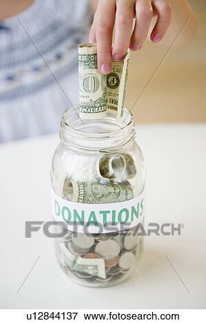 Stock Photo - Close up of girl's (10-11) hand putting dollar bill into jar. Fotosearch