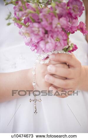 Stock Image - Close up of girl's (8-9) hands holding flowers and rosary beads. Fotosearch