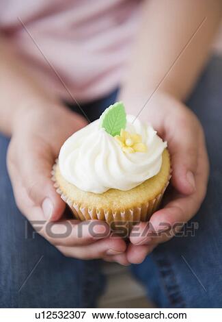 Stock Photo - Close up of girl's (8-9) hands holding cupcake. Fotosearch
